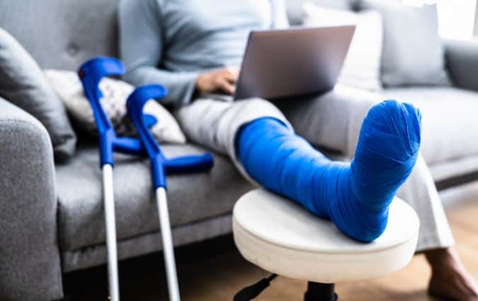 Törött lábbal a kanapén ülő személy laptopozik – a balesetbiztosítás fedezi a váratlan helyzeteket
