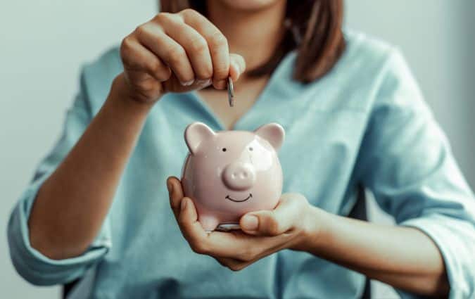 Nő egy malacperselybe helyez pénzérmét, a megtakarításos életbiztosítás jelképeként